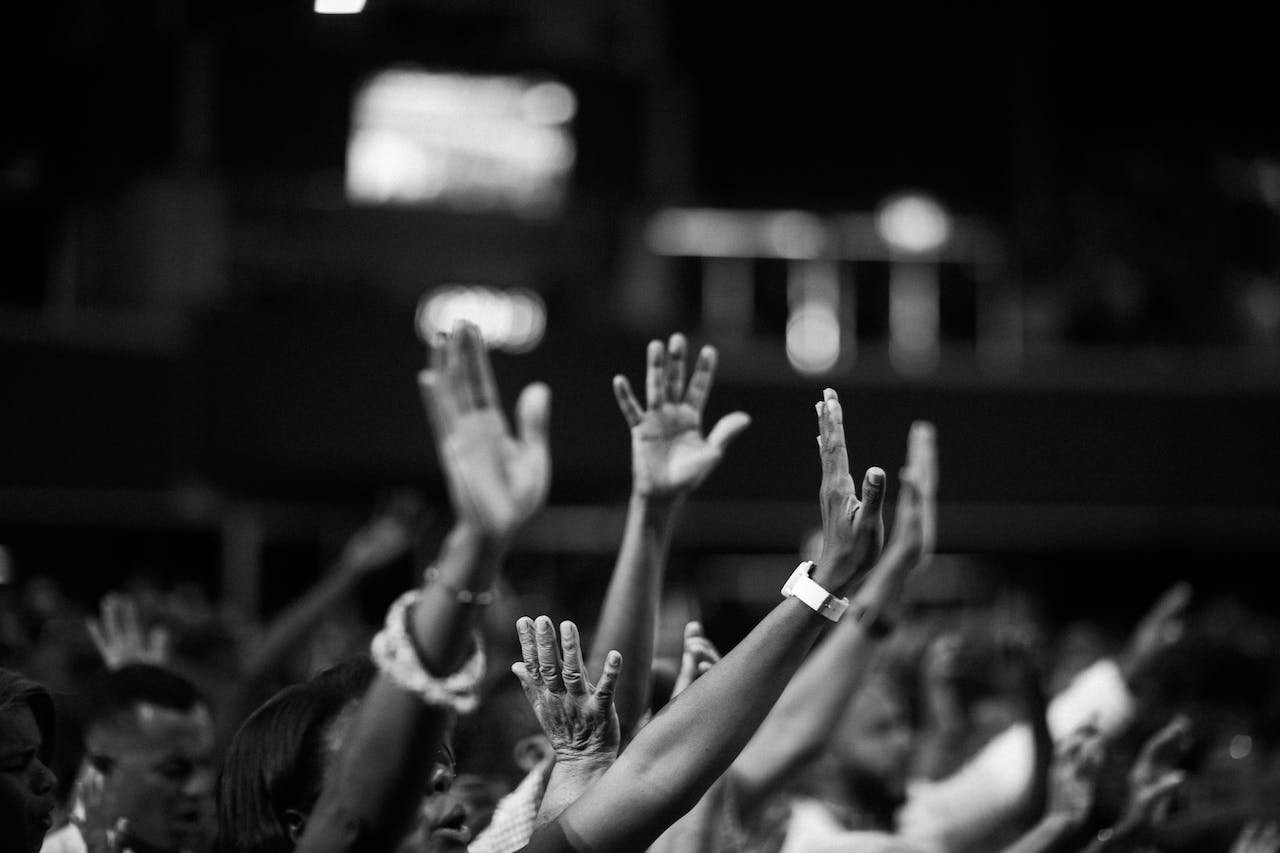 Black and white image of many hands held up in prayer